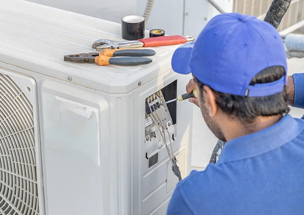 Technician repairing an outdoor air conditioner with service tools nearby