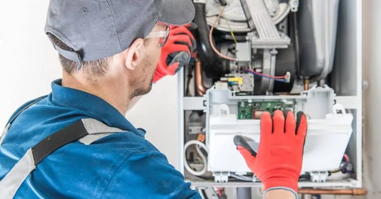 Technician wearing red gloves servicing an open heating appliance